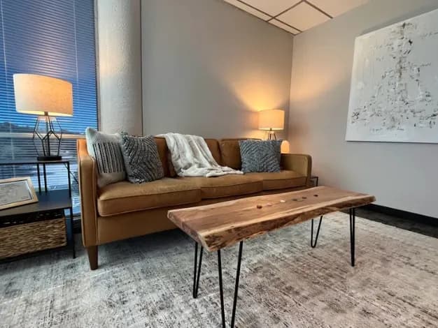 Therapy room with a leather sofa, soft lamplight, and a live-edge wooden table