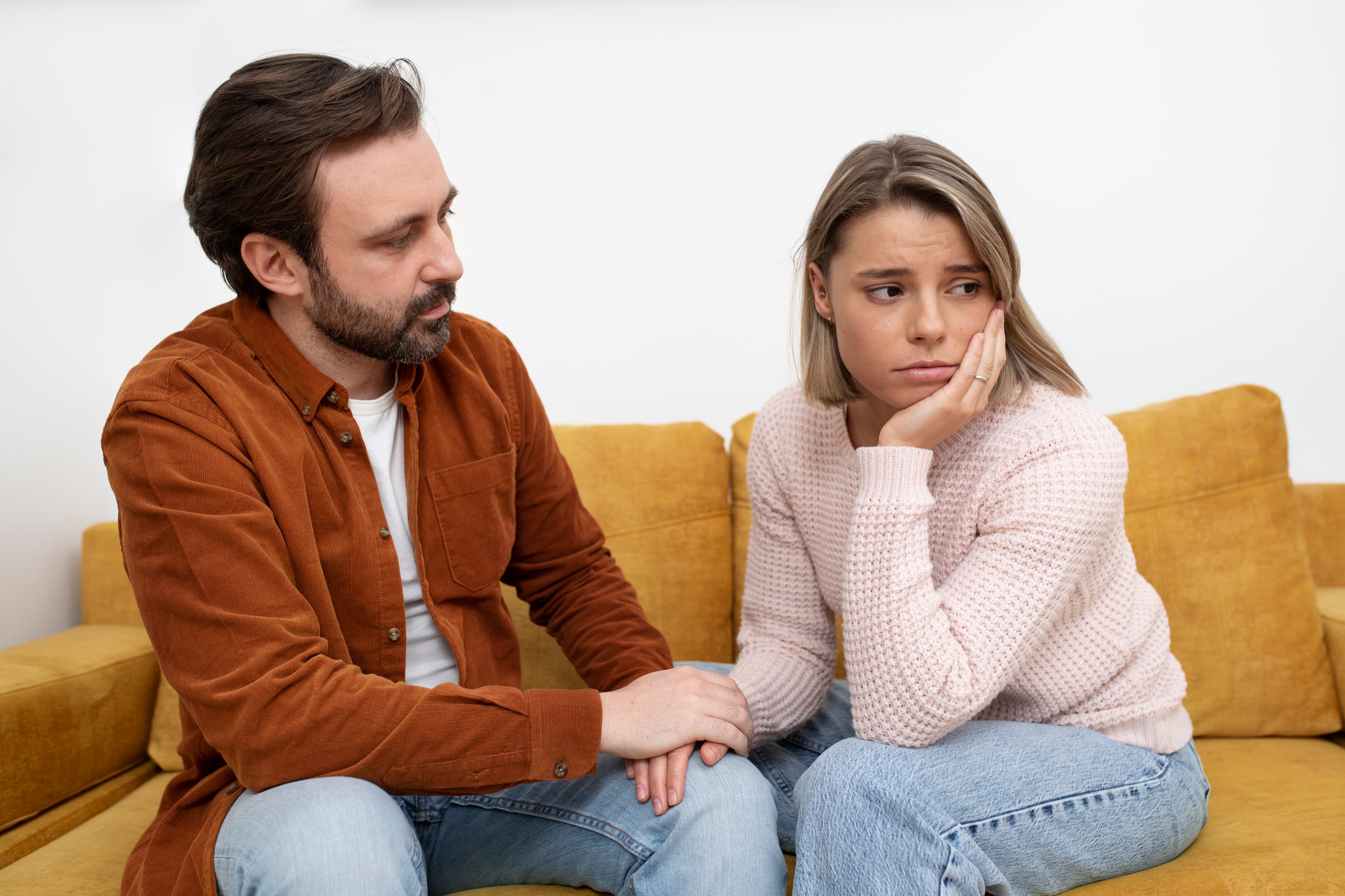 A man on a couch reaching out to comfort a visibly upset woman sitting beside him