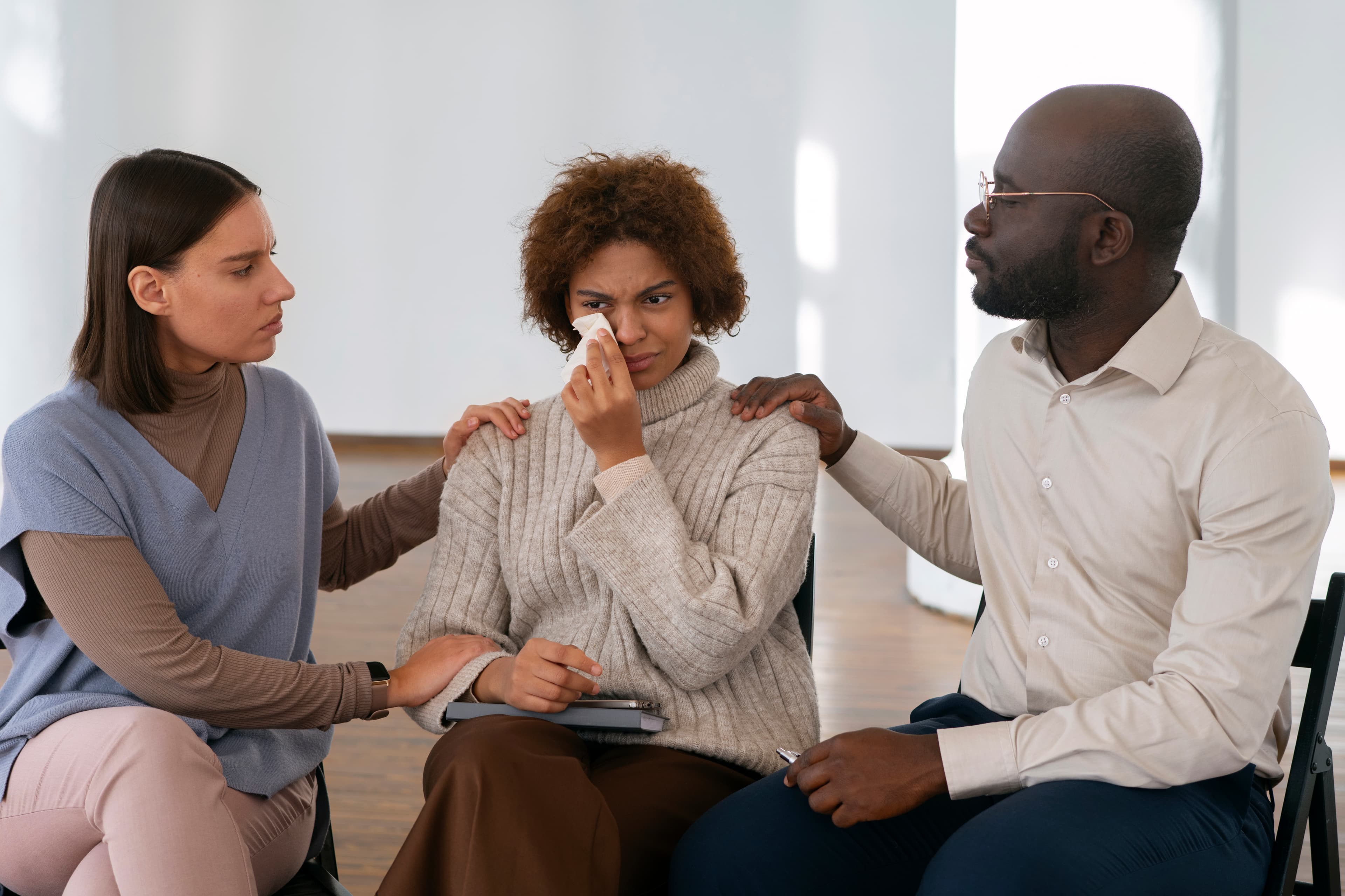 Two people sitting across from each other, one gently holding the other's hands in a supportive gesture